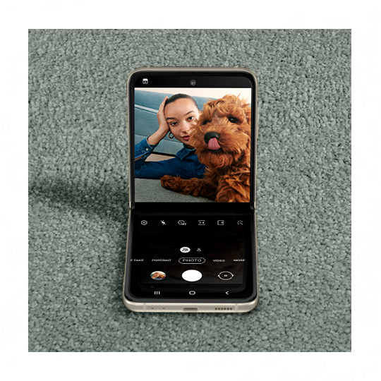 A woman taking a selfie with a puppy licking its nose. Galaxy Z Flip3 5G seen in Flex mode with the Camera app on the Main Screen, and the same photo seen in the viewfinder.