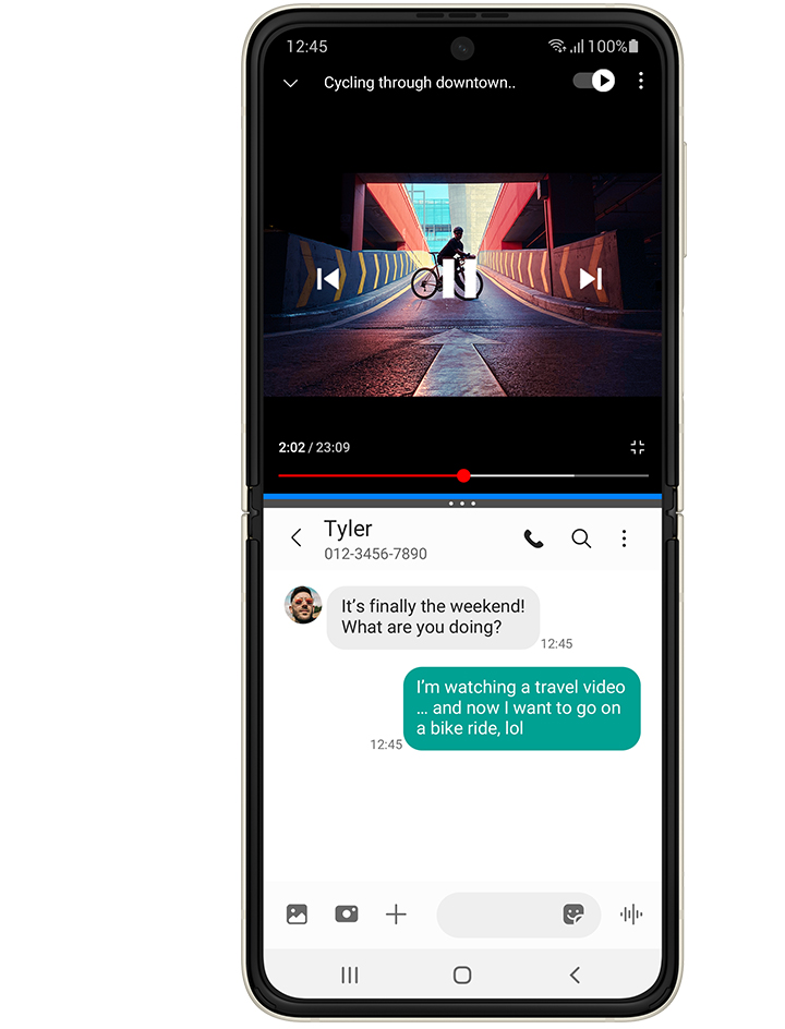 Galaxy Z Flip3 5G unfolded in Multi Active Window, with a YouTube video on top, a video called Cycling Through Downtown and a person standing on a bike on a ramp. The Messages app on the bottom and the received text message from Tyler says "It's finally the weekend! What are you doing?". The sent text message says "I'm watching a travel video... and now I want to go on a bike ride, lol"